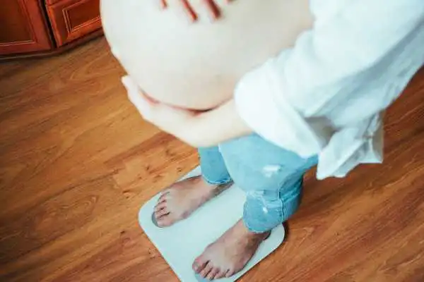 Image of woman weighing herself and experiencing weight gain through pregnancy Burnley